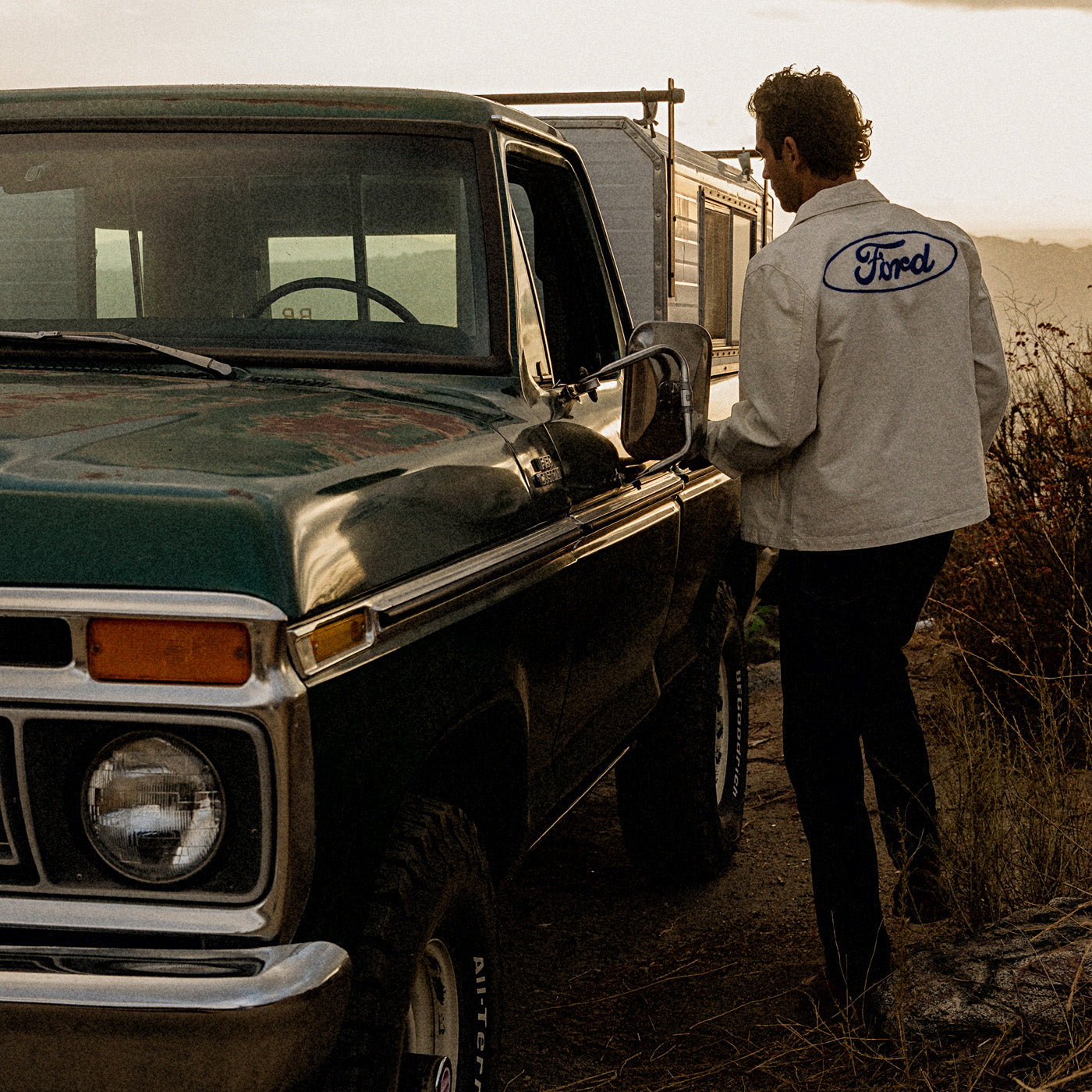 man wearing ford oval jacket getting into green ford bronco outside