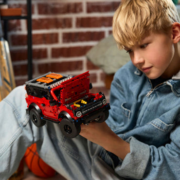 Child playing with a red toy truck in front of a brick wall