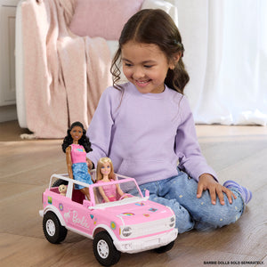 young girl in a purple shirt playing with a pink Barbie Bronco