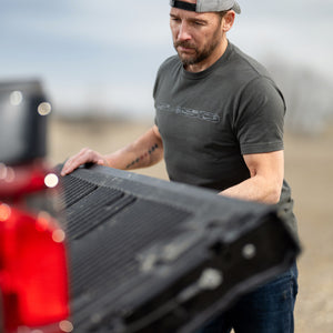 Man adjusting a black truck bed cover outdoors wearing an F-150 shirt