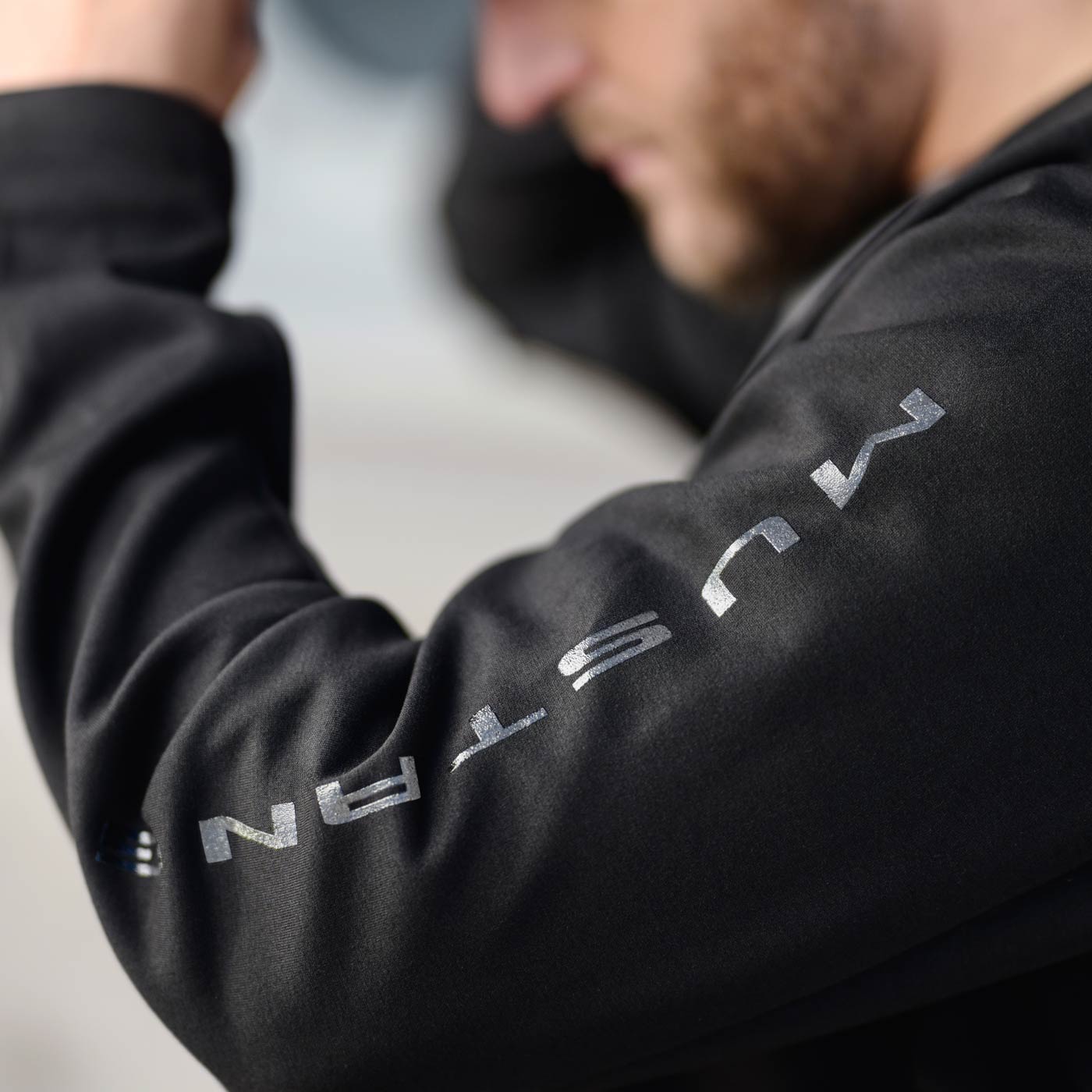 man with left arm up showing mustang text down the sleeve of a black sweatshirt