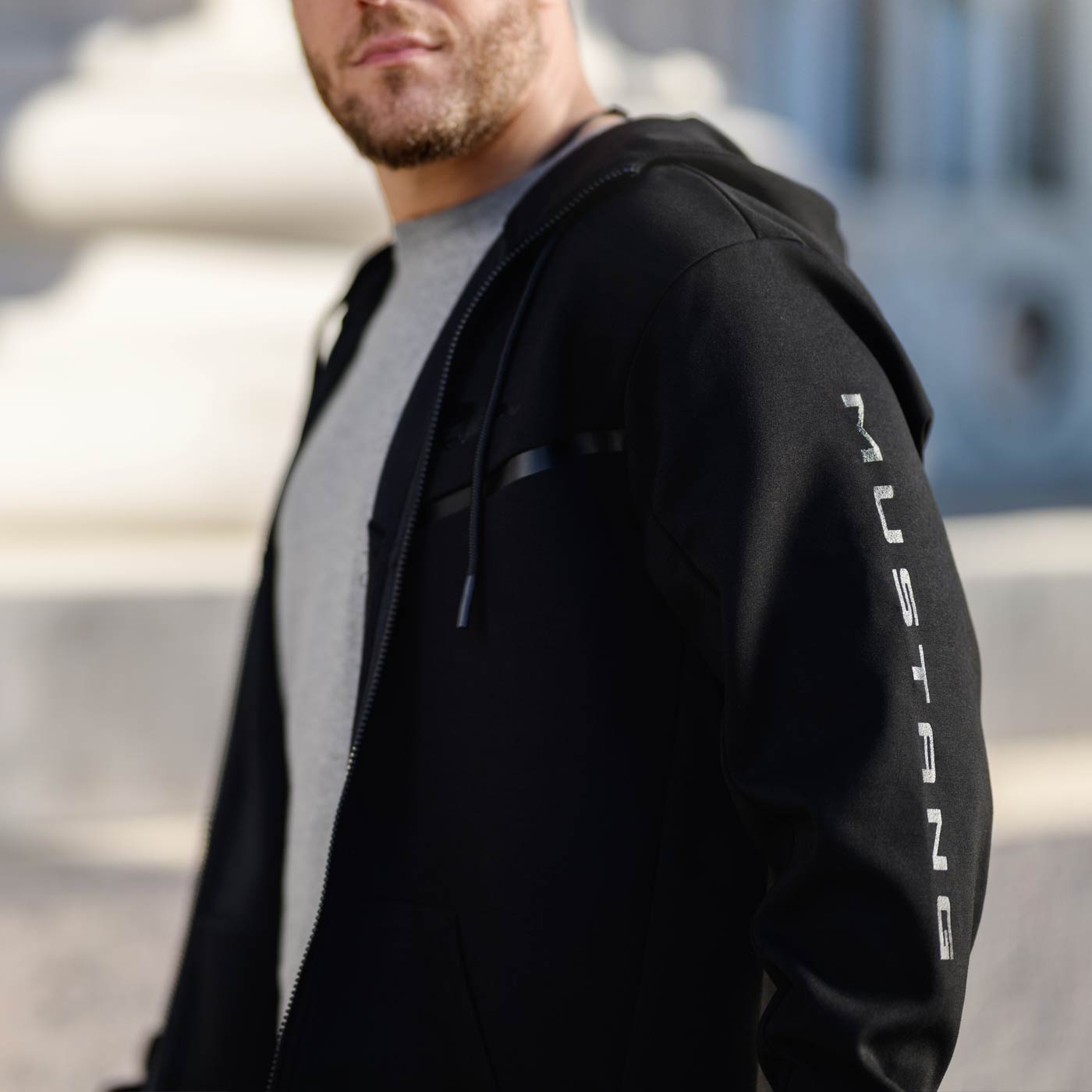 cropped image of mans face with a full zip mustang sweatshirt in black with mustang text down the sleeve