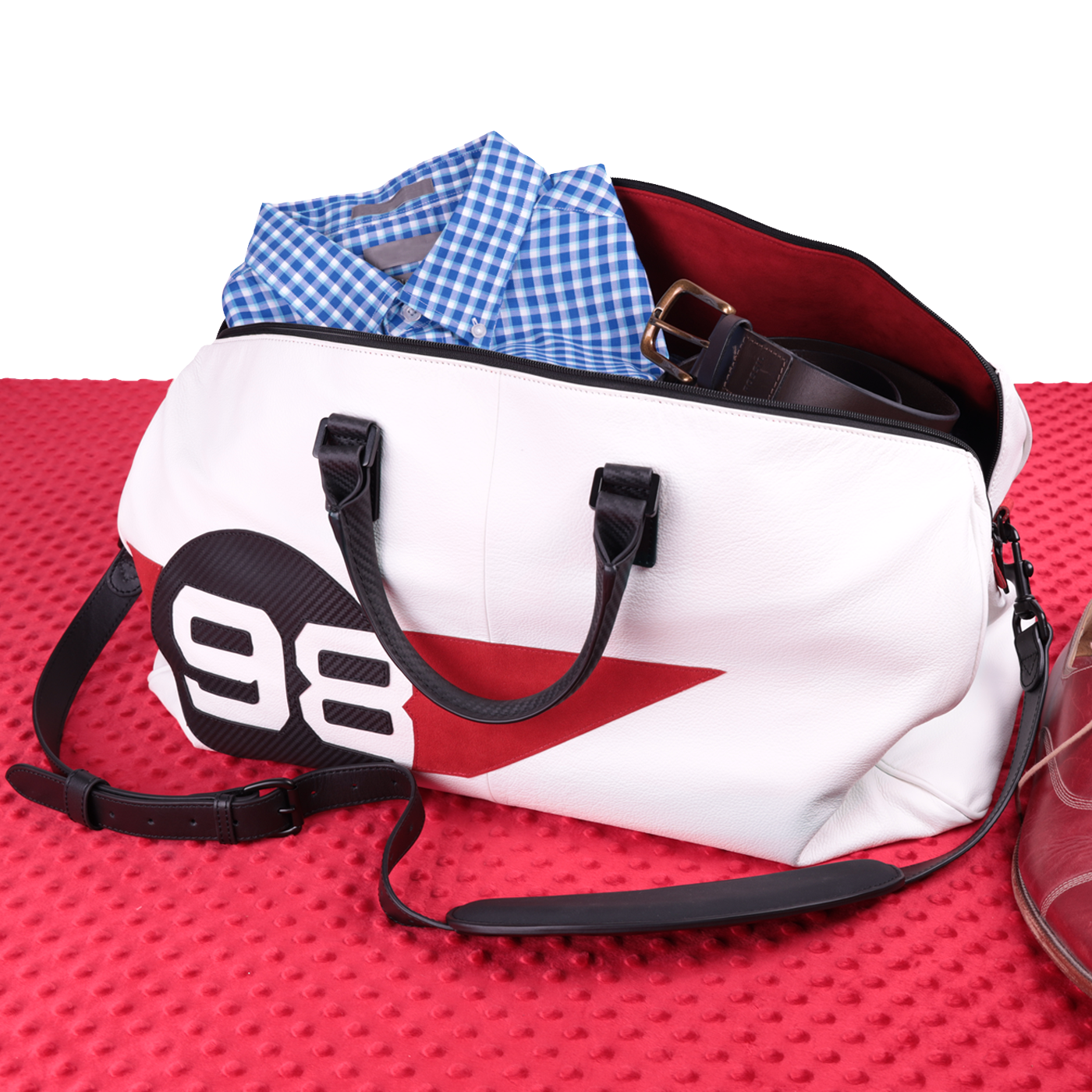 White duffel bag with black straps and a red accent on a red textured surface.