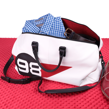 White duffel bag with black straps and a red accent on a red textured surface.