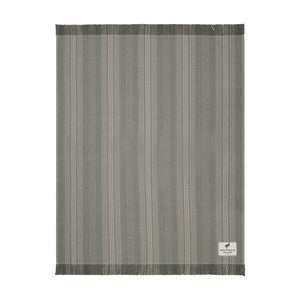 A rectangular woven rug with a vertical stripe pattern in shades of gray, beige, and white, featuring fringed edges and a small white brand label in the bottom right corner.