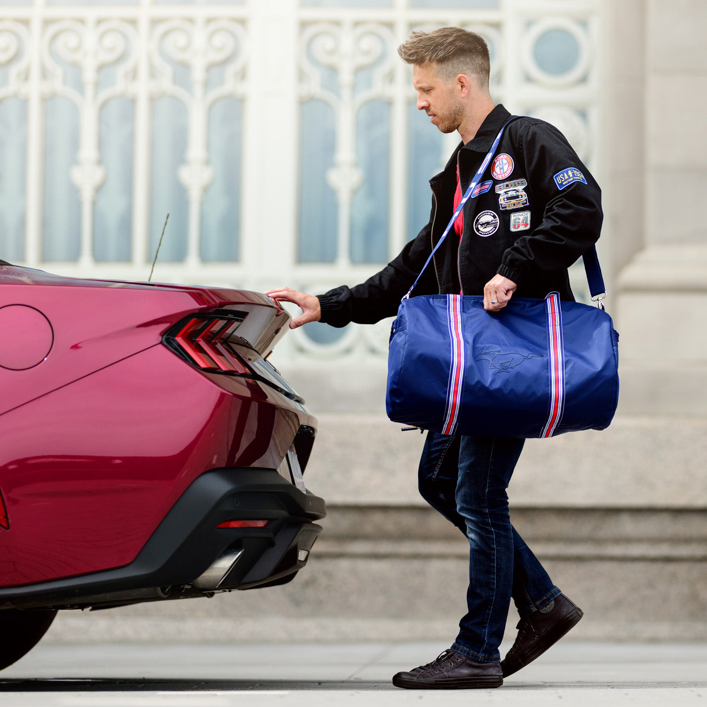 Man with a blue duffel bag opening the trunk of a red car.