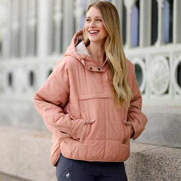 Woman wearing a pink quilted jacket standing outdoors with decorative architecture in the background