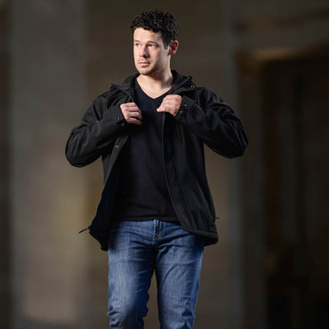 Man wearing a black jacket and blue jeans against a dark background
