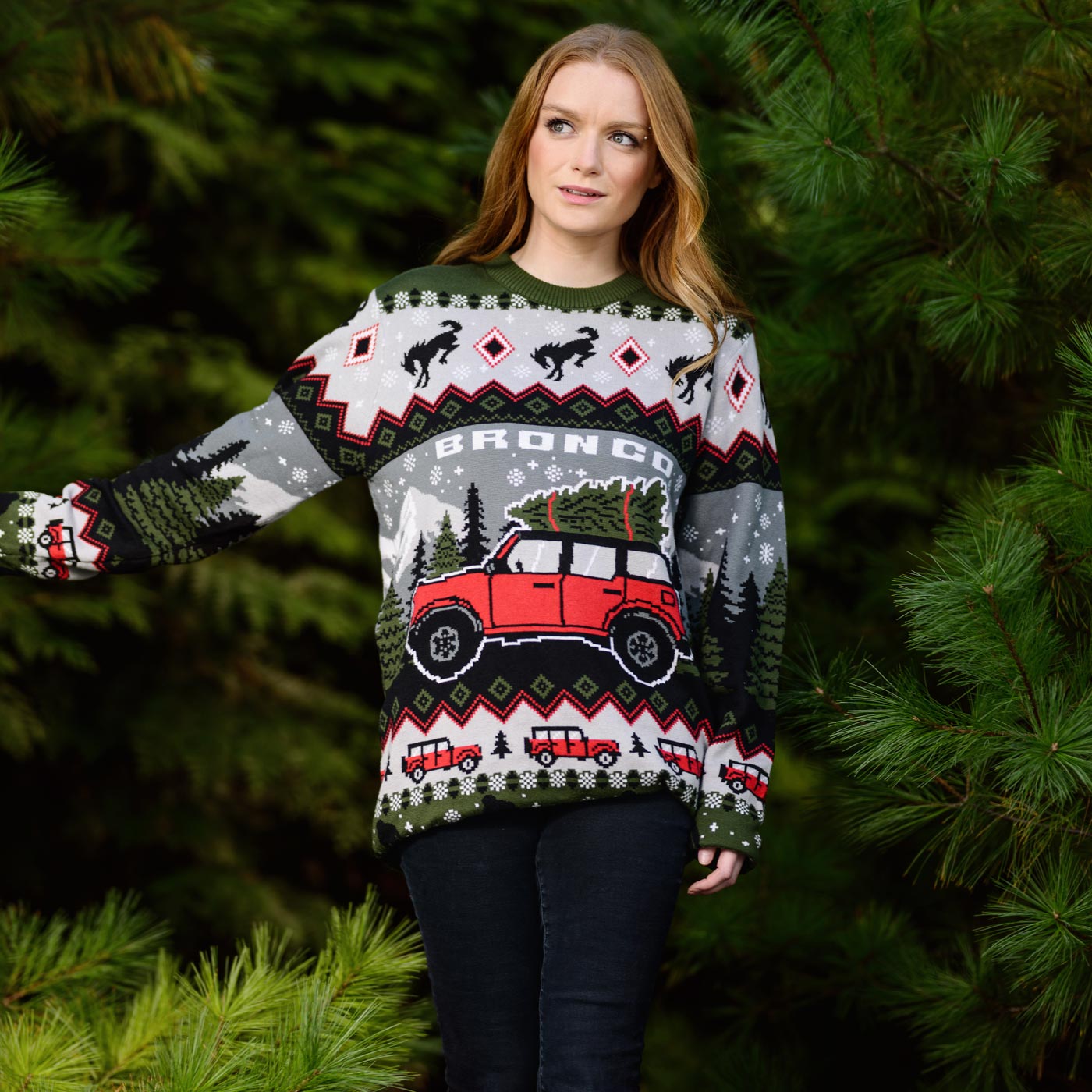 Person wearing a festive sweater with a red ford bronco design, standing in a forest setting.