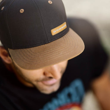 man wearing a black and tan brimmed hat with a bronco leather patch