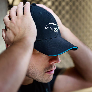 Person wearing a black cap with a logo, adjusting it on their head.