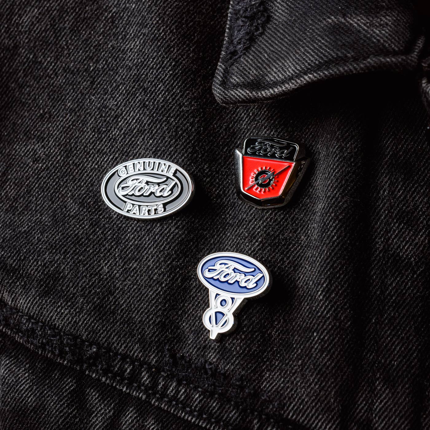Three Ford brand pins on a black denim background