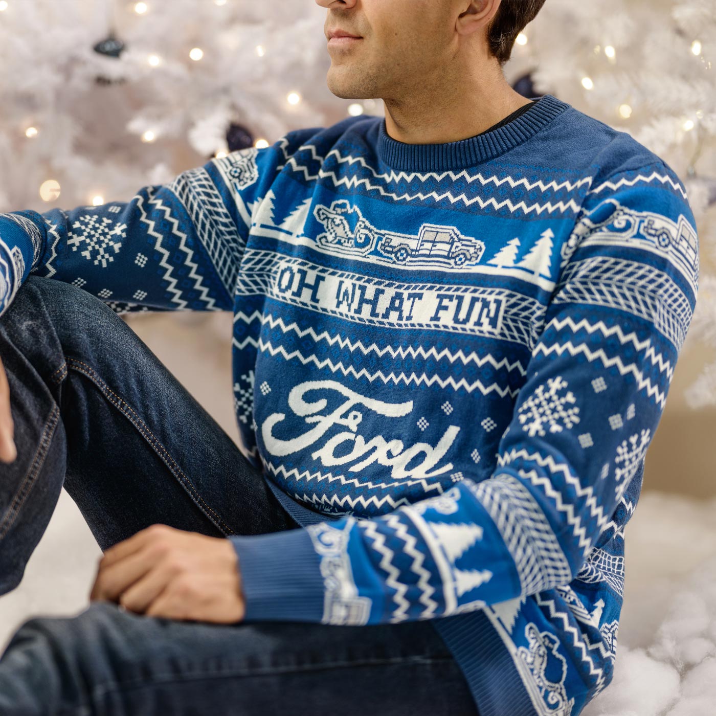 Person wearing a blue sweater with white patterns and text, sitting against a blurred festive background.