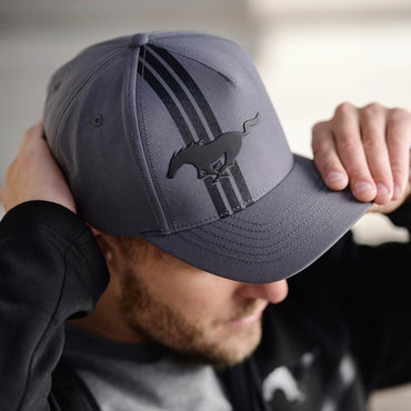 Person wearing a gray cap with a MUSTANG  logo, holding it on their head.