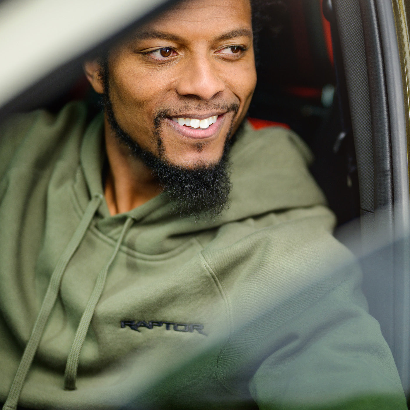 Man wearing a green hoodie with 'Raptor' logo sitting inside a vehicle.
