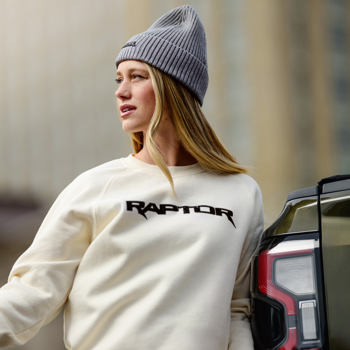 Person wearing a white sweatshirt with 'Raptor' text, standing next to a vehicle.
