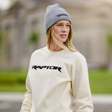 Person wearing a white sweatshirt with 'Raptor' logo and a gray beanie outdoors.
