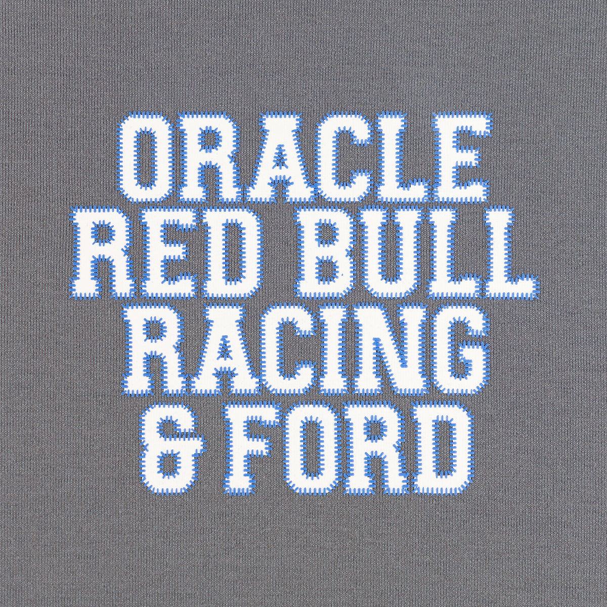 Close-up of a gray knit fabric with large white block letters outlined in blue reading 'ORACLE RED BULL RACING & FORD'.
