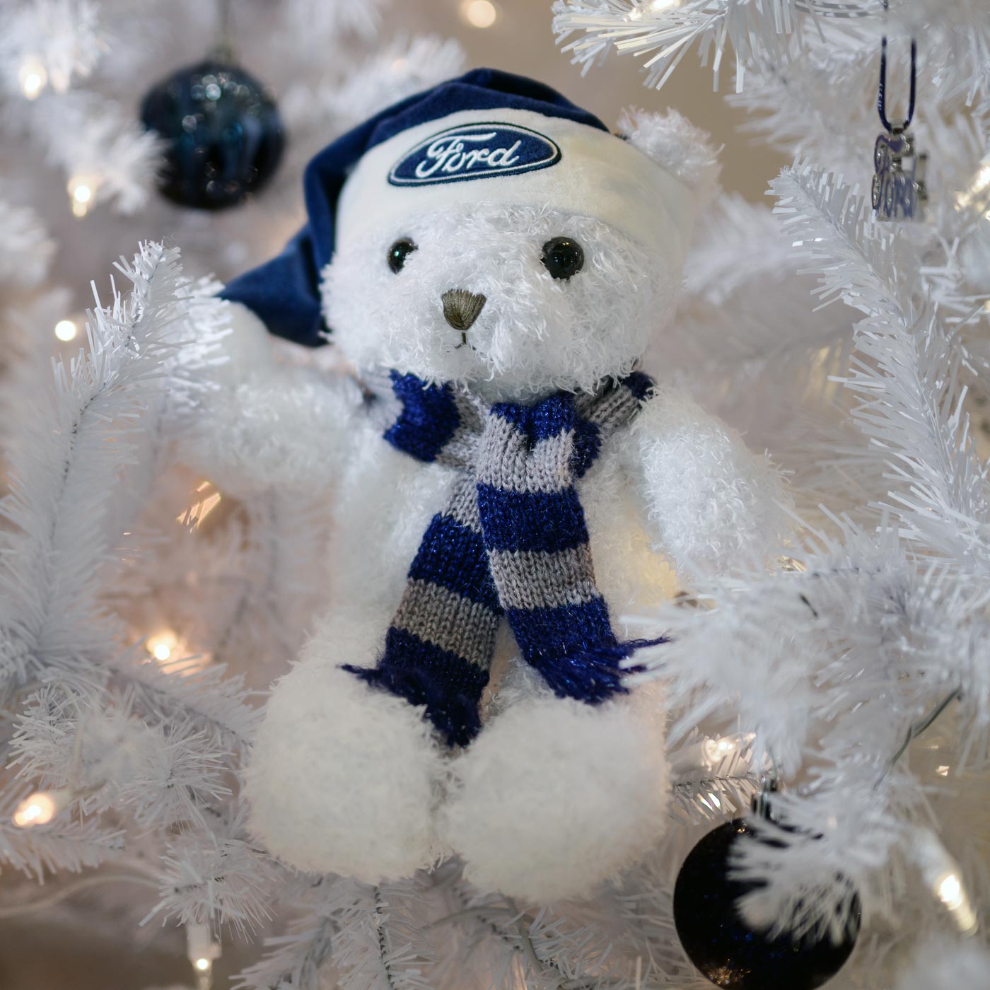 White teddy bear with blue scarf and hat on a white Christmas tree