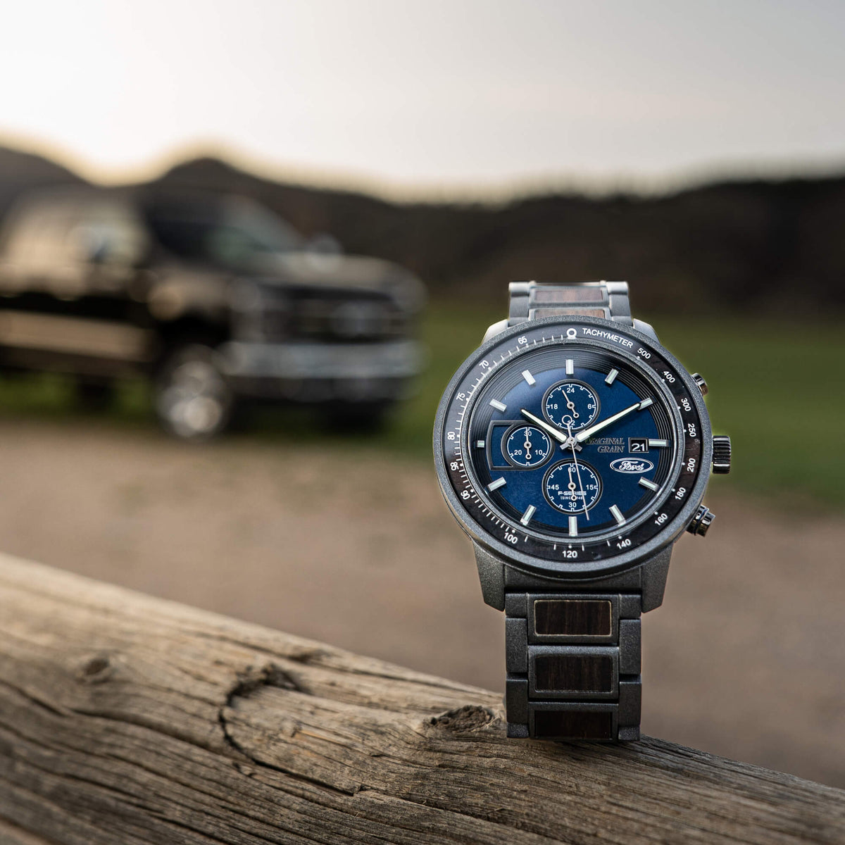Wristwatch with blue dial on a wooden surface, blurred background of a vehicle and landscape