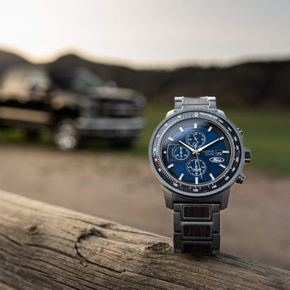 Wristwatch with blue dial on a wooden surface, blurred background of a vehicle and landscape