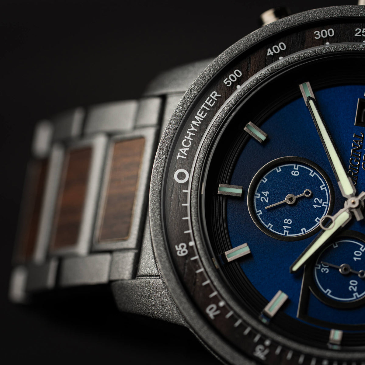 Close-up of a watch with a blue face and metallic strap on a dark background