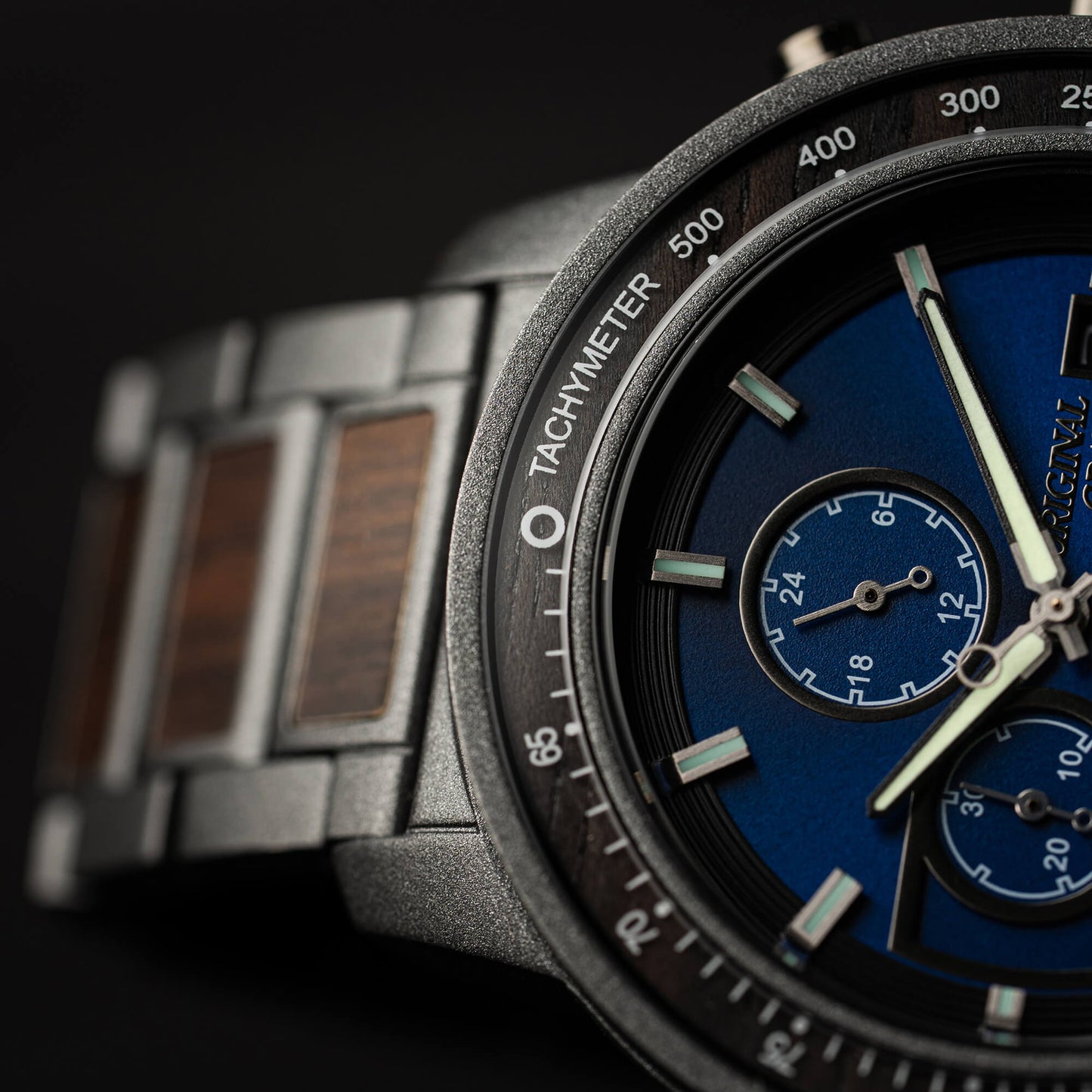 Close-up of a watch with a blue face and metallic strap on a dark background