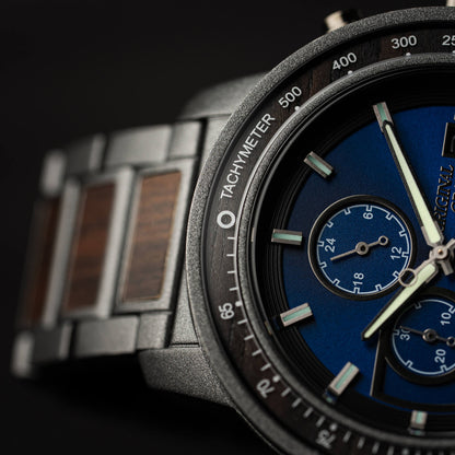 Close-up of a watch with a blue face and metallic strap on a dark background