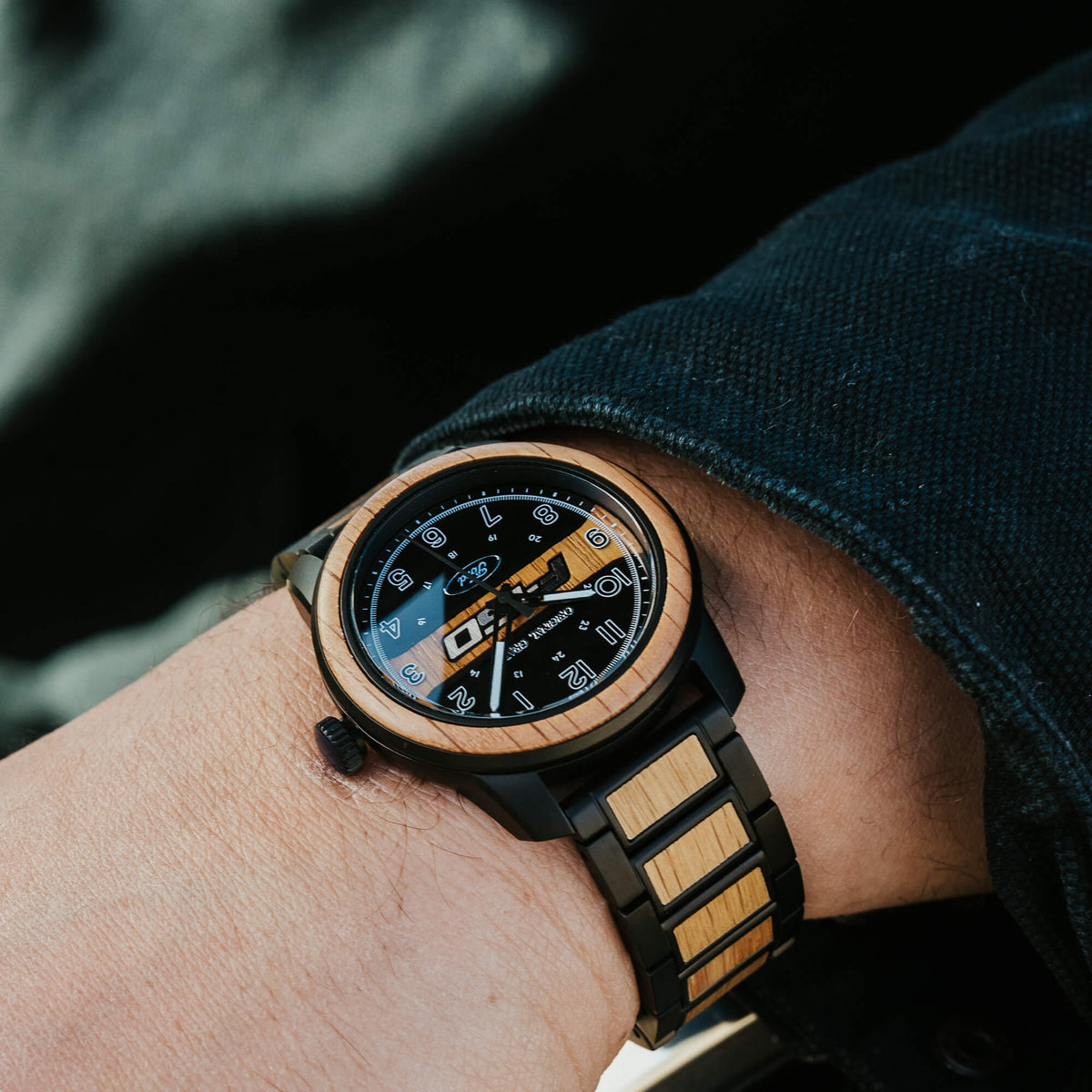 Wooden watch with black strap on wrist against a dark background