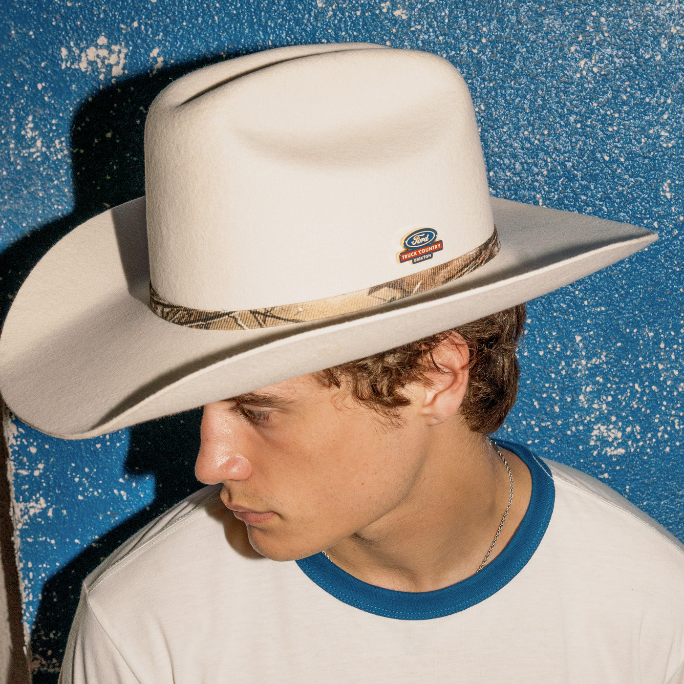man in front of blue background with white ford truck country cowboy hat