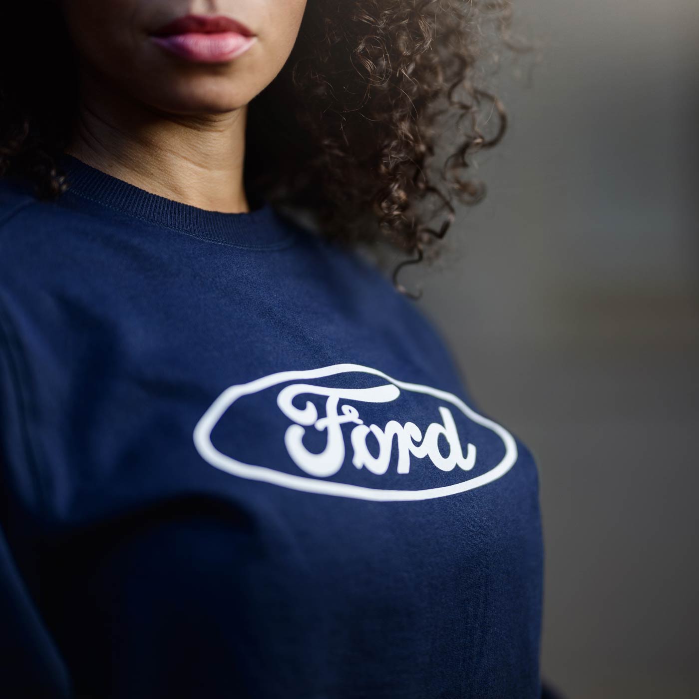 cropped image of women's face with curly black hair standing in navy blue sweatshirt with white for script and oval on front