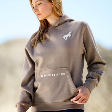 Red head women wearing a brown hoodie with a horse on left shoulder and bronco on front pocket