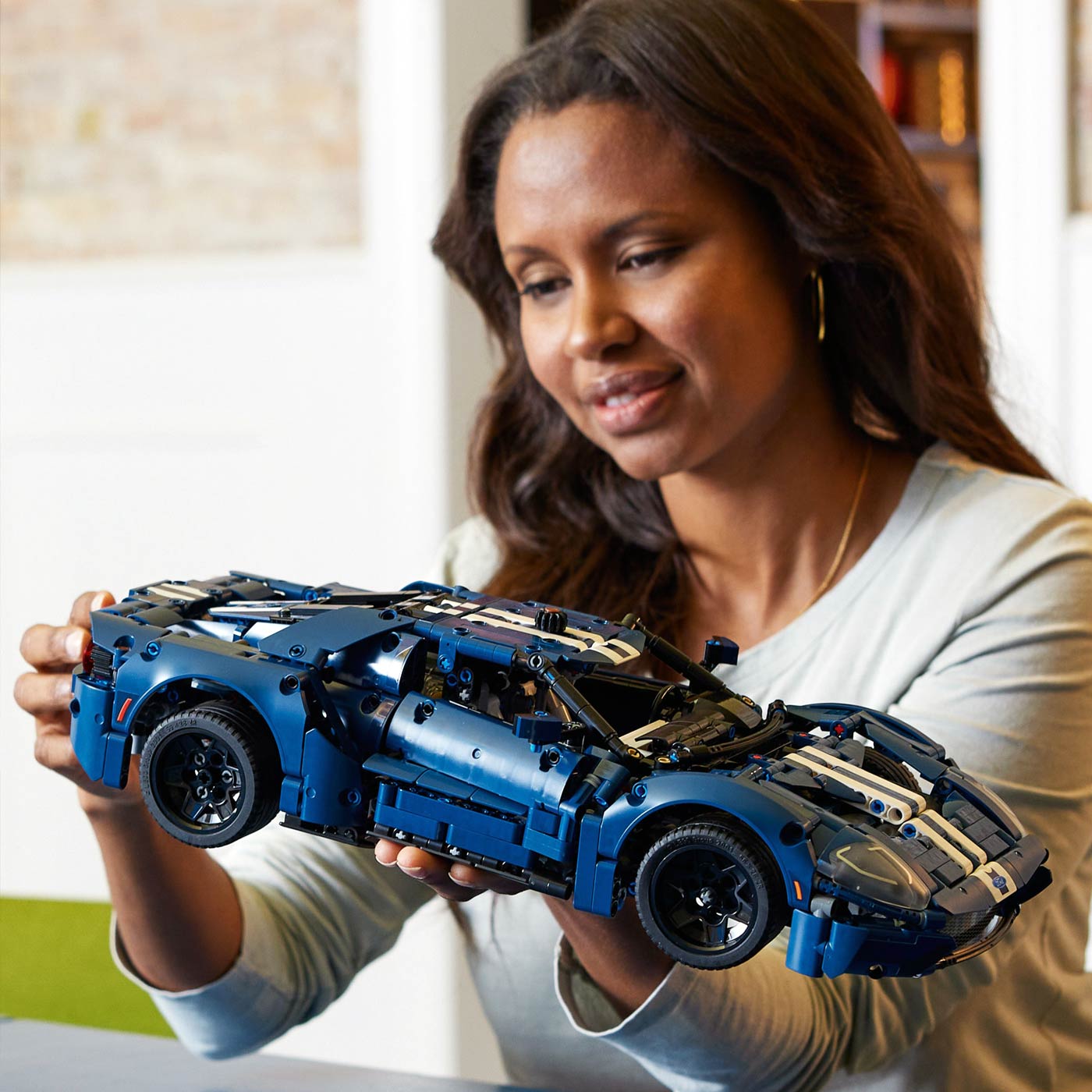 Woman holding a blue and black LEGO model of a car indoors