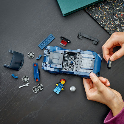 Person assembling a blue toy car model with various pieces on a dark surface