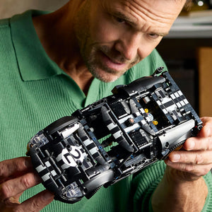 Man holding a complex model made of interlocking bricks, possibly a LEGO set.