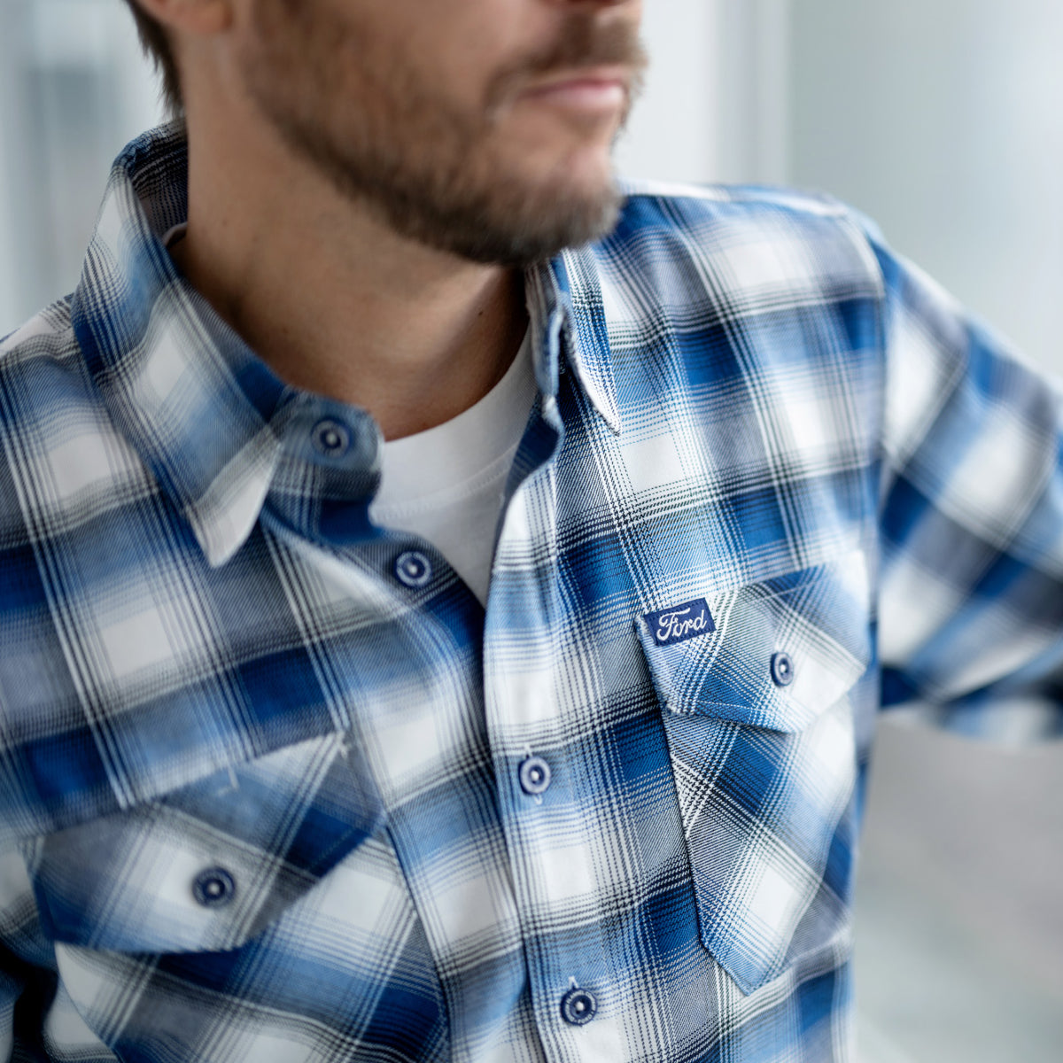 Man wearing a blue and white plaid shirt with a Ford logo on a blurred background