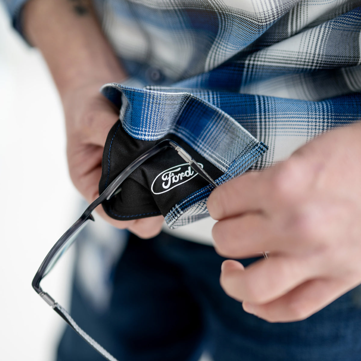 Person holding a black Ford-branded eye glasses cleaner with a blurred background