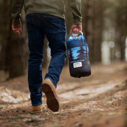 Person walking in a forest holding a black and blue bag with a tree design.