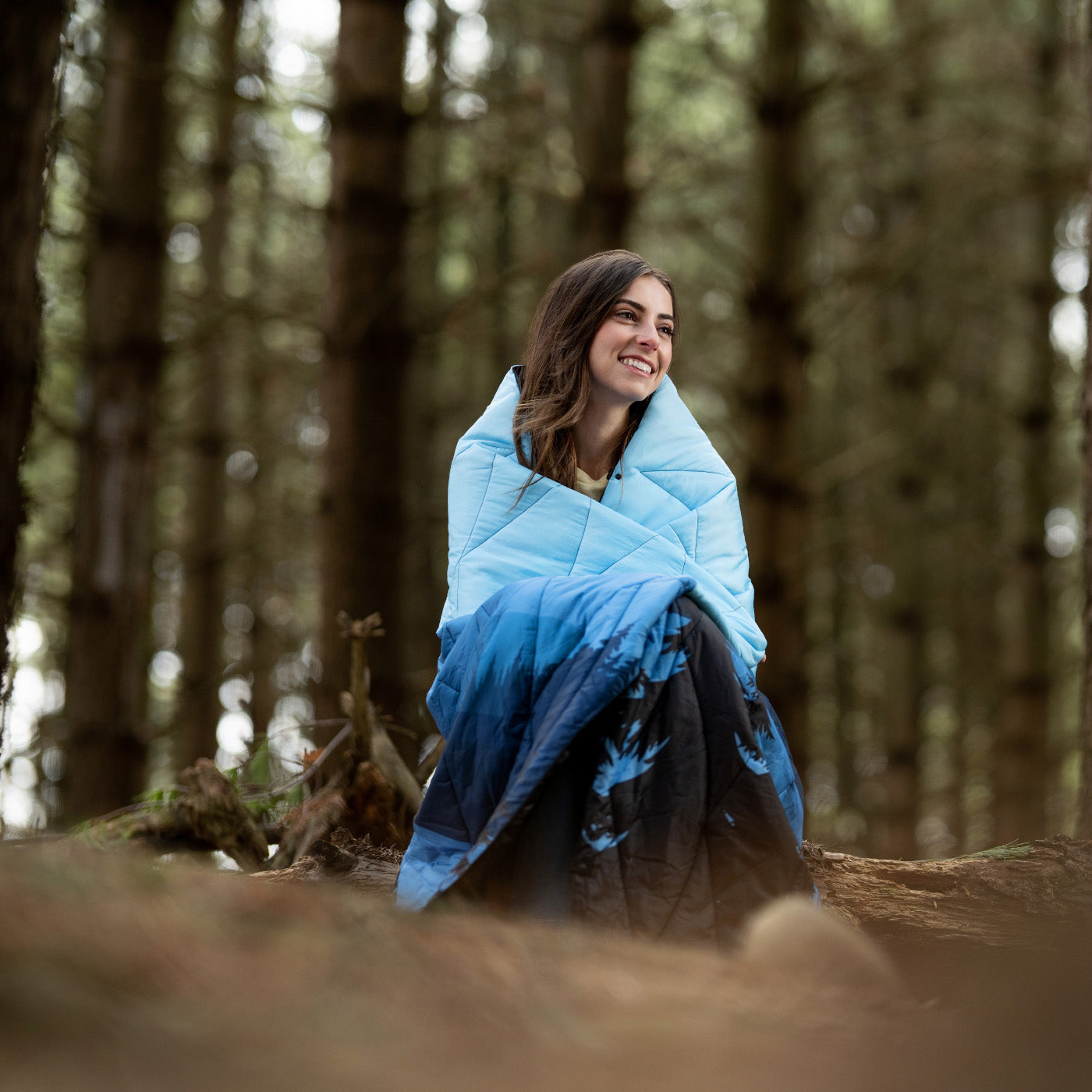 Woman wrapped in a blue quilt sitting in a forest