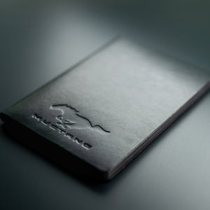 Black leather notebook with 'Mustang' embossed logo on a dark background