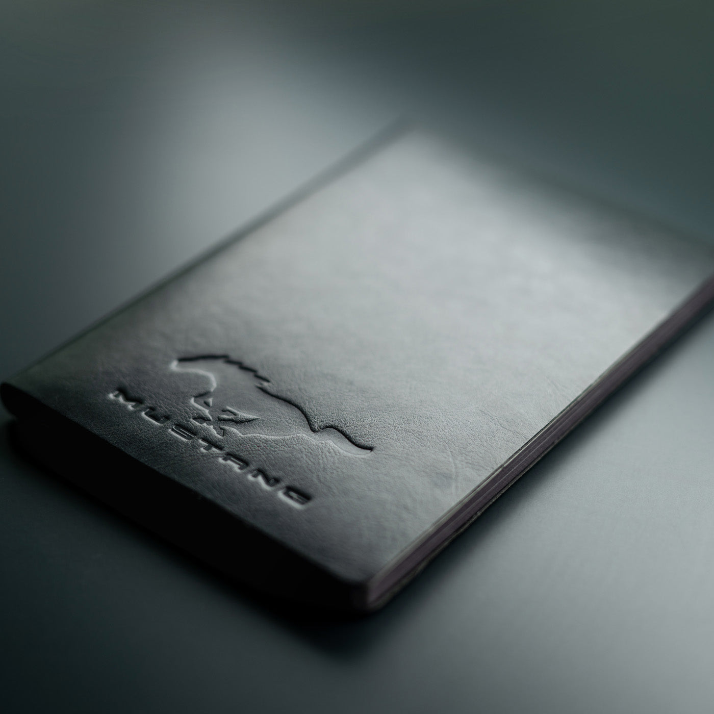 Black leather notebook with 'Mustang' embossed logo on a dark background