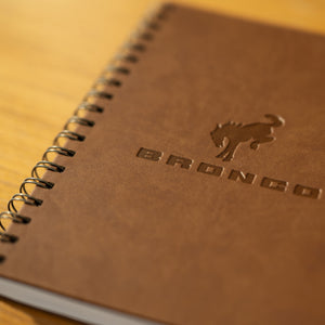 Brown notebook with 'Bronco' branding on a wooden surface
