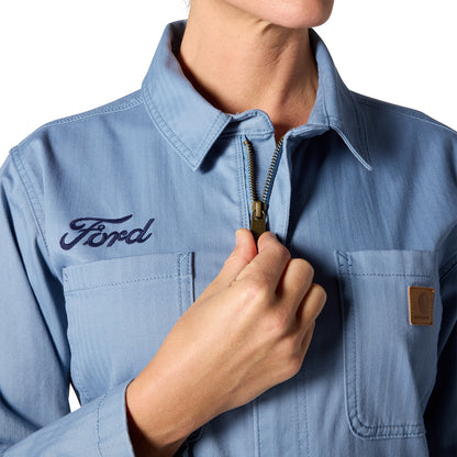 A close-up of a person wearing a light blue zip-front work shirt with a visible Ford logo on the chest and a brown Carhartt brand patch on the pocket.