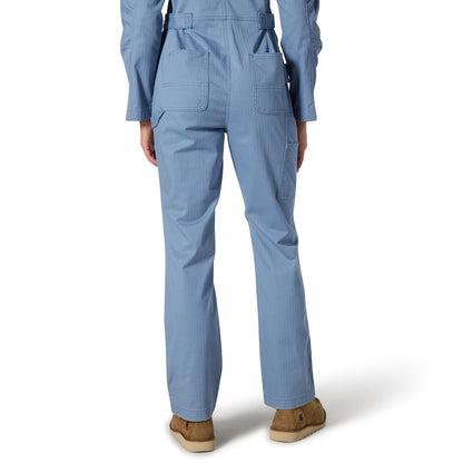 A person shown from the back wearing light blue scrub-style overalls with belt loops, flap back pockets, and straight legs, paired with tan slip-on shoes against a clean white studio background.