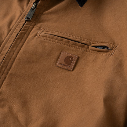 Close-up of a brown Carhartt jacket showing a zippered pocket with a brown leather Carhartt logo patch.
