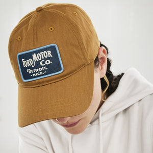 A person wearing a brown baseball cap with a blue and white 'Ford Motor Co. Detroit, Mich.