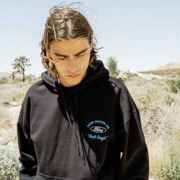 A man wearing a black hoodie with a blue 'Ford Motor Co. Built Tough' logo on the chest, standing outdoors in a desert landscape.