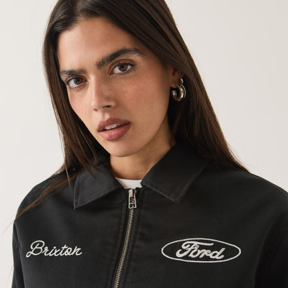 A close-up of a woman wearing a black zip-up jacket with white embroidered logos reading 'Brixton' on the left chest and 'Ford' on the right chest, against a plain light background.