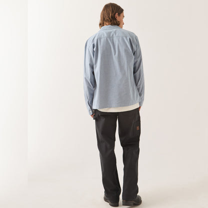 A model shown from the back wearing a light blue long-sleeve button-up shirt, black pants, and black shoes, standing against a plain off-white studio background.