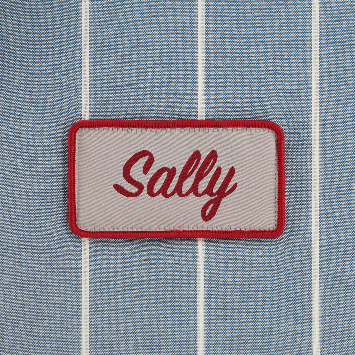 Patch with 'Sally' text on a blue striped fabric background